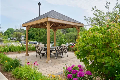 Wooden gazebo with a table and chairs surrounded by flowering plants