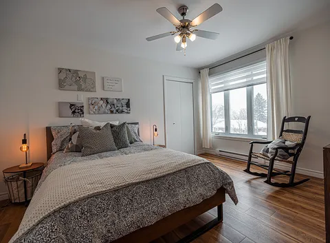 Bedroom with a patterned bedcover, ceiling fan and dark rocking chair
