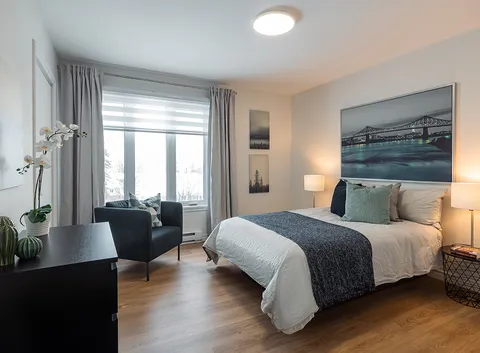 Bedroom with a double bed, dark armchair and a bridge photograph above the headboard