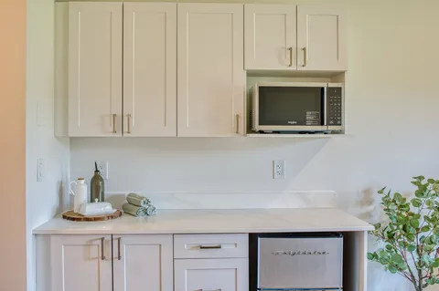 White kitchenette with cabinets, counter and microwave.