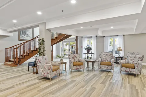Lobby seating beside an open wooden staircase and tall windows.
