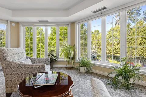 Sunroom with armchairs and broad windows overlooking trees.