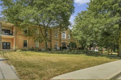 Yellow-brick residence beside a lawn, mature trees and a sidewalk