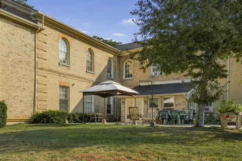 Rear of a yellow-brick residence with patio chairs and a canopy beside a lawn
