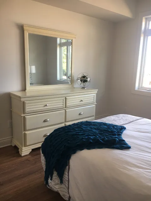 Bedroom with a white dresser, mirror and a bed with a dark blue blanket