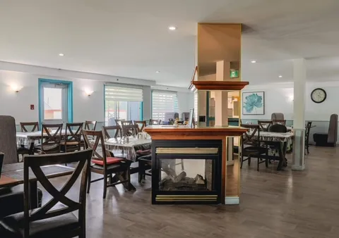 Dining tables and chairs around a glass-sided fireplace beside large windows