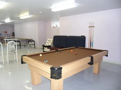 Billiard table beside chairs, cue racks, a folding table and fluorescent lights