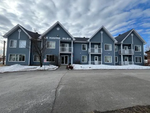 Blue two-storey building with balconies, a glass entrance and snow beside the driveway