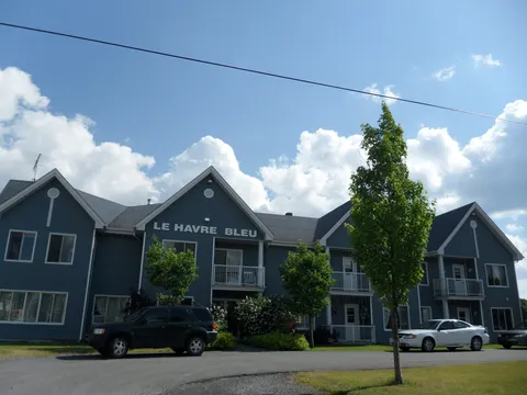 Blue two-storey building with balconies, trees and parked cars