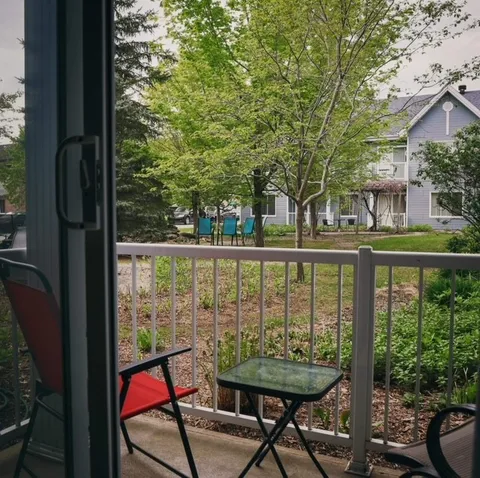 Small balcony with two chairs, a table and a view of trees and a blue building