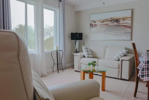 White sofa and armchair beside a glass coffee table, large window and landscape painting