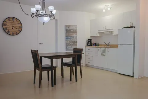 Dining table and two chairs beside white kitchenette cabinets and a refrigerator