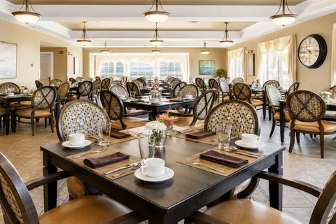 Dining room with set tables, patterned chairs, pendant lights and large windows.