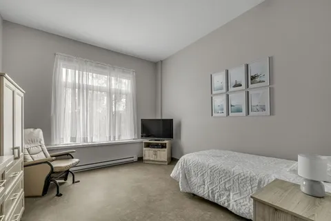 Bedroom with a single bed, reclining chair, television and framed coastal artwork