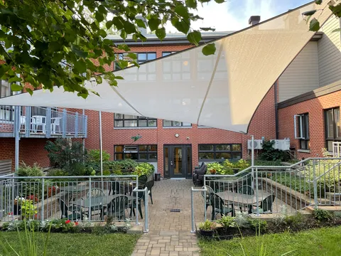 Courtyard patio with tables, chairs, planted beds and shade sails.