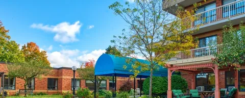 Brick building with balconies and a blue entrance canopy beside landscaped beds