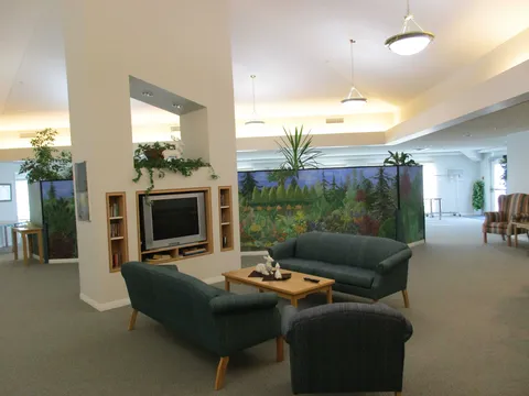 Lounge with green sofas, a television, coffee table and painted forest panels.