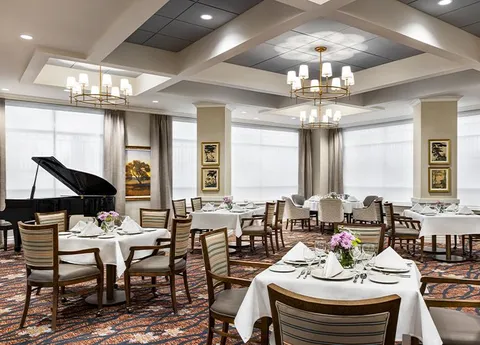 Dining tables with white tablecloths beside a grand piano and large windows