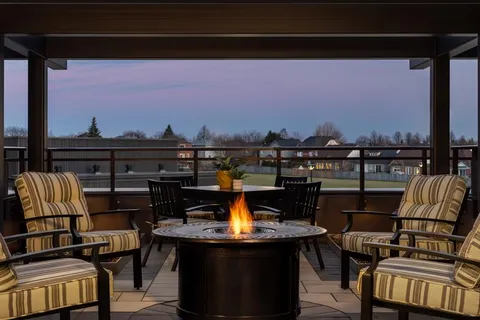 Covered terrace with striped chairs around a round fire table at dusk