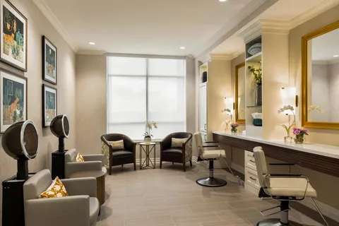 Salon chairs and hair dryers beside mirrors and two armchairs