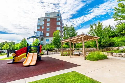 Playground slide and wooden pergola beside lawns, paths and planted terraces