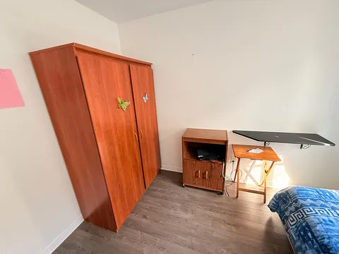 Bedroom corner with wooden wardrobe, television and over-bed table.