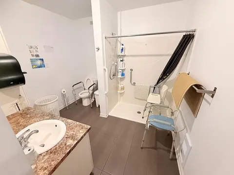 Accessible bathroom with shower chair, grab bars, toilet and sink.