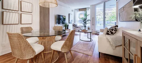 Suite dining and living area with a table, sofa and broad windows.