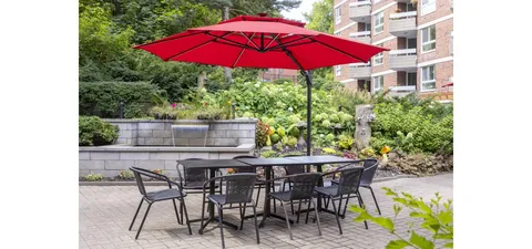 Garden patio with tables and chairs beneath a red umbrella.