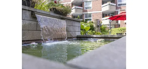 Garden fountain beside stone walls and plants.