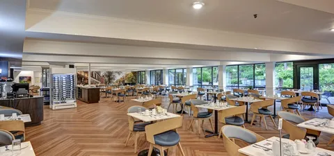 Dining room with set tables and large windows overlooking trees.