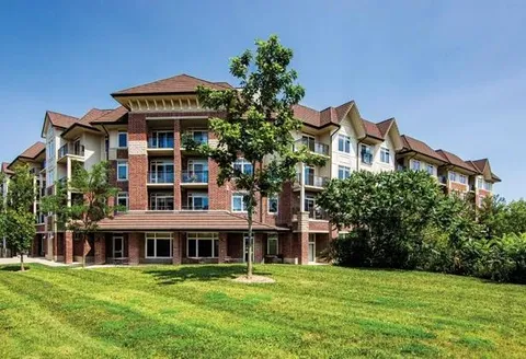 Residence facade with balconies beside a lawn and trees.