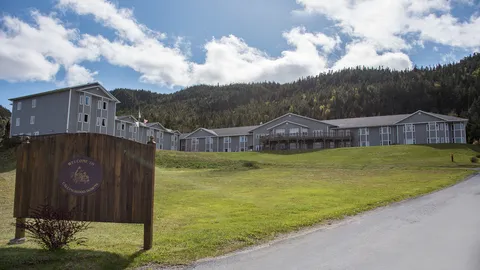 Long building with a sloping lawn, trees, a driveway and a residence sign