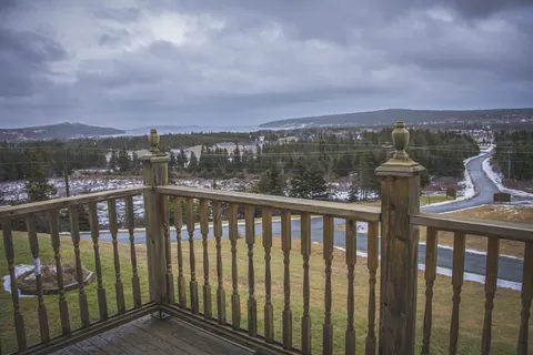 Wooden balcony railing overlooking a lawn, trees and nearby buildings
