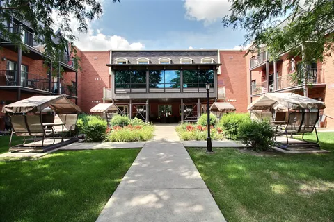 Courtyard with covered patio swings, lawns, flower beds and a walkway to the brick building