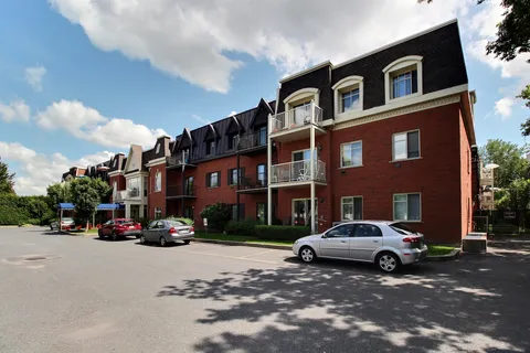 Red brick residential building with balconies, a blue entrance canopy and parked cars