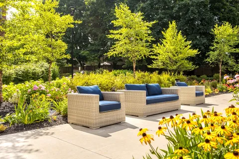 Wicker sofa and armchairs with blue cushions beside trees and flowering garden beds