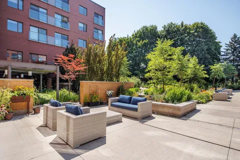 Patio seating with blue cushions beside raised flower beds and a brick building