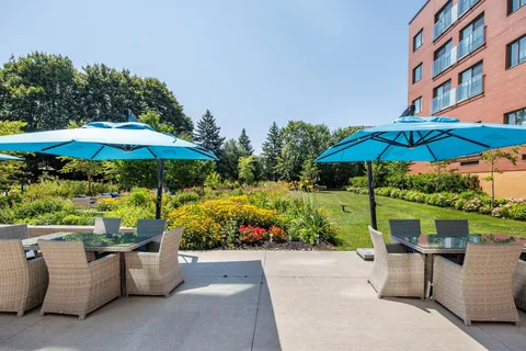 Patio tables and wicker chairs under turquoise umbrellas beside a flower garden