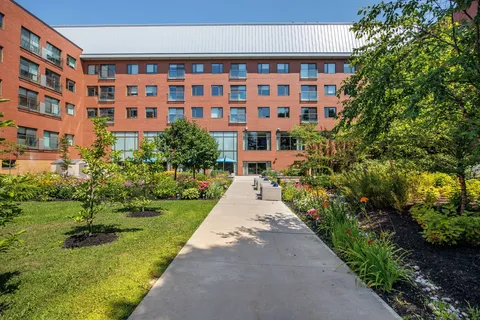 Brick residence around a garden with a paved path, flower beds and patio seating