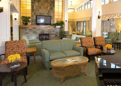 Atrium lounge with armchairs, a stone fireplace and tall windows.