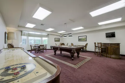 Room with a pool table, shuffleboard table and small tables with chairs