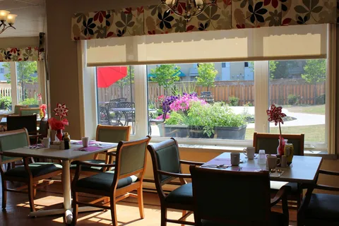 Dining room with tables and chairs beside windows overlooking flowers.
