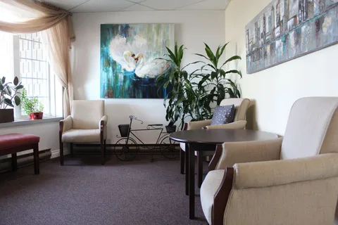 Seating area with upholstered chairs, a table, artwork and plants.