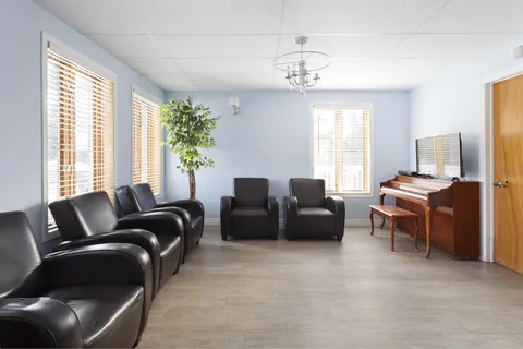 Room with black armchairs, a piano, a television and tall windows