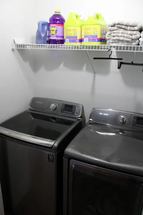 Laundry area with a washing machine, dryer and a shelf of cleaning supplies.