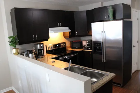 Kitchen with dark cupboards, a stove, microwave, refrigerator and double sink.