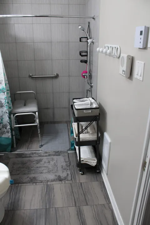 Bathroom with a shower seat, grab rails and a towel trolley.