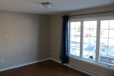 Unfurnished bedroom with wooden flooring and a large window.