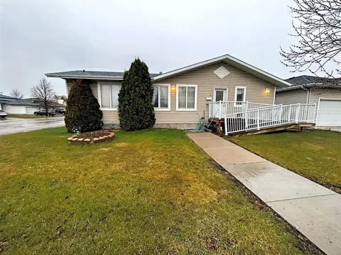 Single-storey residence with beige siding, evergreen shrubs and a ramp with white railings.